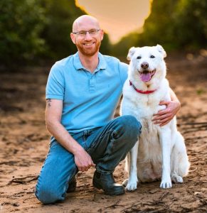 גיא תיכון מומחה באילוף כלבים בטיול בשדה עם כלב לבן